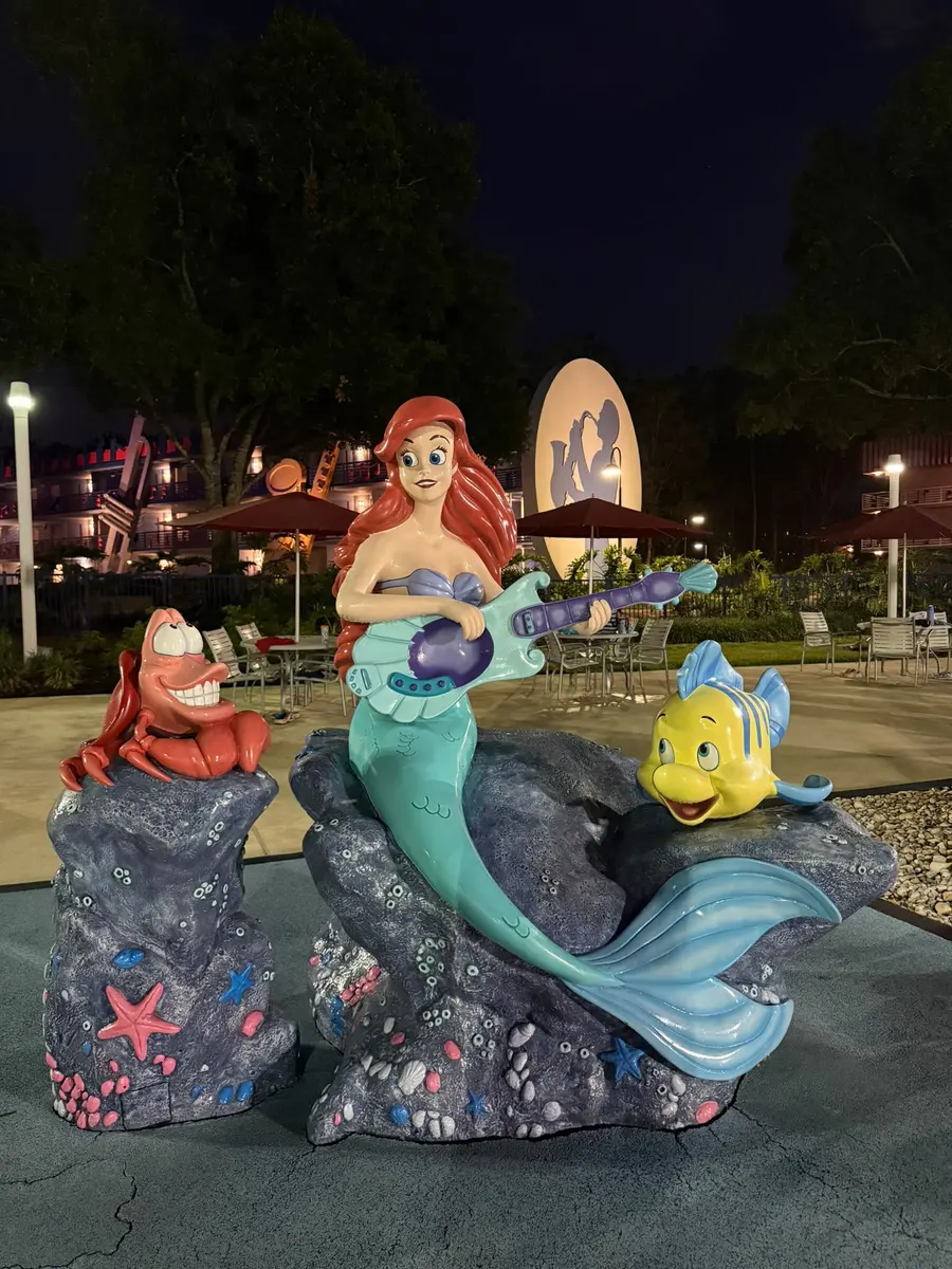 Estatua de Ariel junto a una de las piscinas del hotel Disney All-Star Music Resort de noche