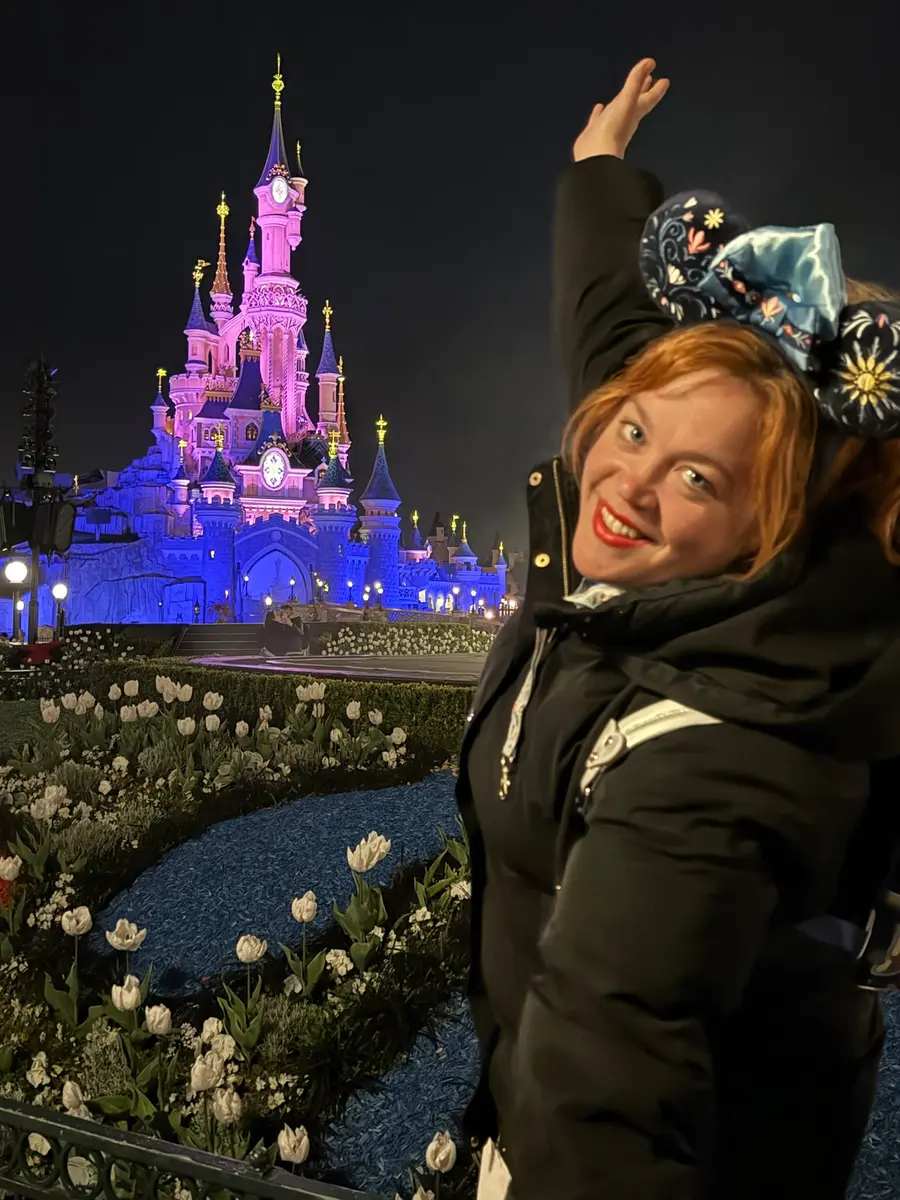 Lara, agente Disney oficial, frente al castillo de la Bella Durmiente de Disneyland Paris iluminado de noche