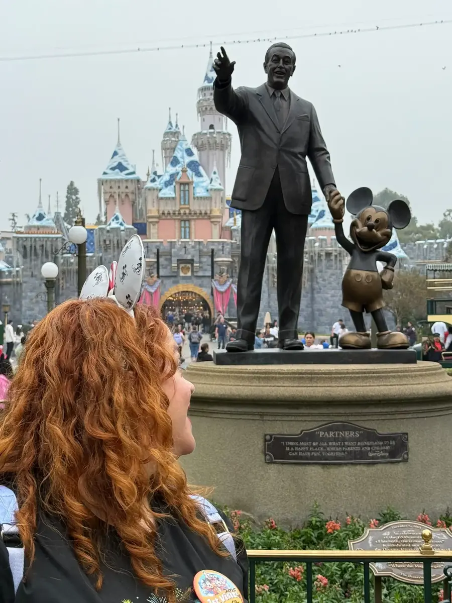 Lara, agente Disney oficial, frente a la estatua de Walt y Mickey y el castillo de Disneyland California